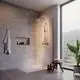Duschsystem von Ideal Standard mit klaren Glaswänden, Thermostat, Handbrause und Wandablage. Sicht auf Fenster und Pflanze im modernen Badezimmer.